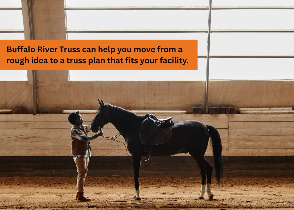Horse and rider inside an indoor arena with high ceilings supported by steel trusses.